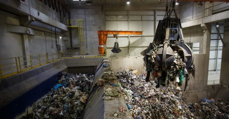 Mechanical claw hand grabbing pile of mixed waste, deposited in the waste treatment plant depot, separation and treatment. Waste disposal, waste management, reuse, recycle and recovery concept.